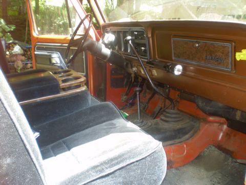 1979 Ford Bronco - The interior of an orange truck shows velour seats and a wood-grain dashboard, consistent with a 1979 model.