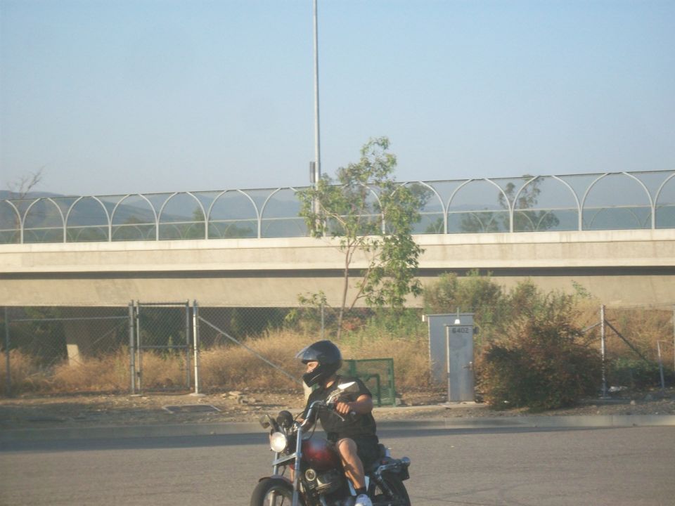Guy on a motorcycle wearing a helmet, riding past a highway overpass