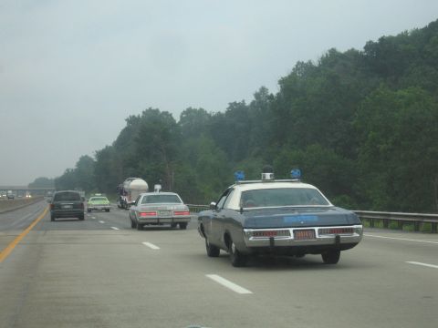 1991 Ford Crown Victoria - Police car with light bar driving on a highway with other traffic.