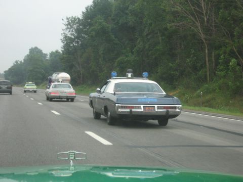 1991 Ford Crown Victoria - A police car with blue lights is seen from behind on a highway, with other vehicles in traffic.