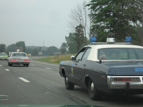 1991 Ford Crown Victoria - A police car with a light bar drives on the highway, with other vehicles visible.