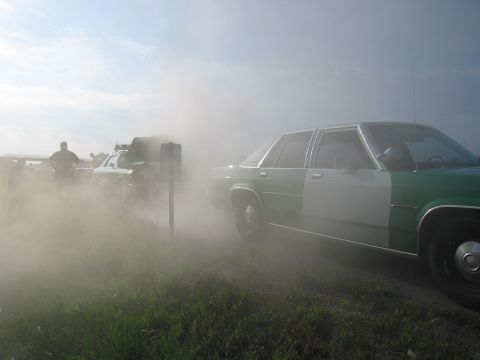 1991 Ford Crown Victoria - A two-tone sedan is seen in a dust cloud with other vehicles and people in the background.