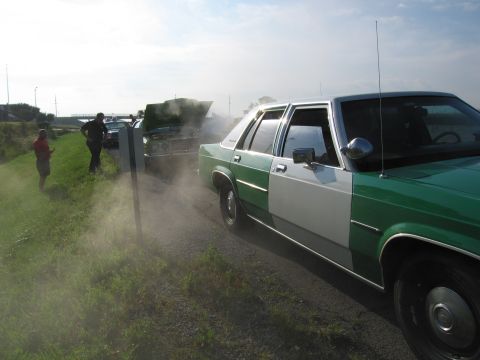 1991 Ford Crown Victoria - A two-tone sedan is parked on the side of the road, with another vehicle having its hood open in the background.