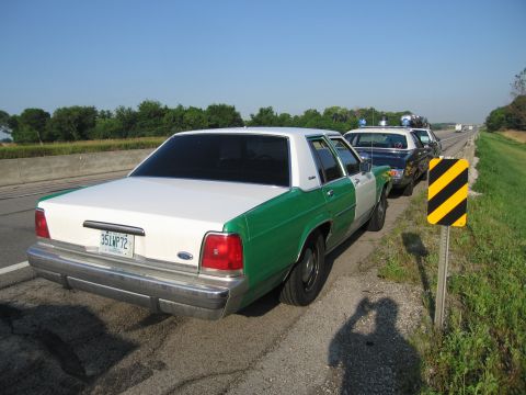 1991 Ford Crown Victoria - A line of police cars, including a 1991 Ford Crown Victoria, are stopped on the shoulder of a highway.