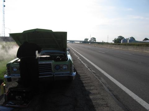 1991 Ford Crown Victoria - Car trouble on the highway; steam billows from the engine compartment as a person attempts repairs.