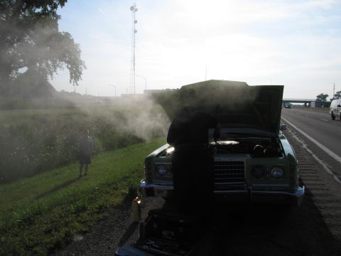 1991 Ford Crown Victoria - A person inspects a car that is emitting a large amount of steam on the side of a highway.
