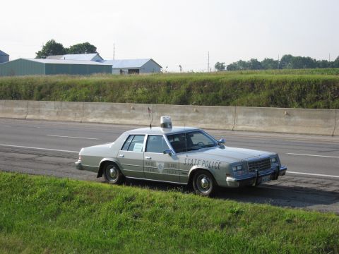 1991 Ford Crown Victoria - A light-colored sedan with 'Rhode Island State Police' markings is parked on the shoulder of a highway.