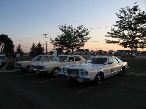 1991 Ford Crown Victoria - Several older model police cars are parked in a lot at dusk.