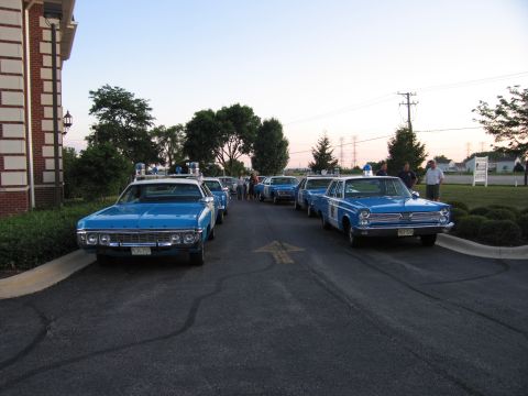 1991 Ford Crown Victoria - A line of vintage police cars are parked outside a building under a clear sky.