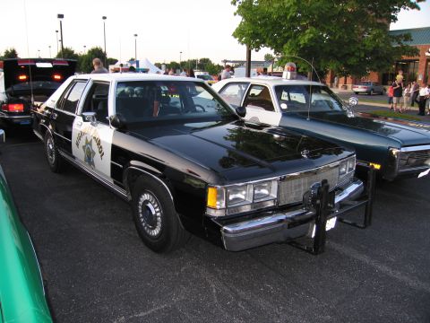 1991 Ford Crown Victoria - A black and white police car is parked next to another police car, with people in the background.