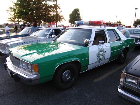 1991 Ford Crown Victoria - A sheriff's department vehicle with a light bar is parked in a lot next to a state police car.