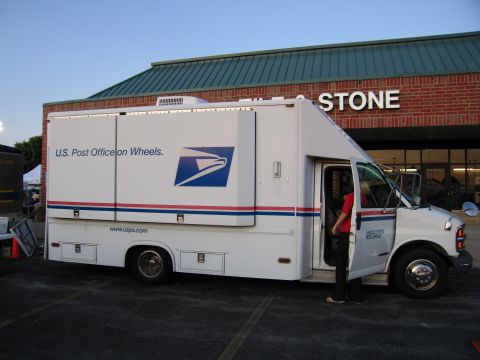 1991 Ford Crown Victoria - A USPS mail truck is parked outside a building with 'STONE' visible on the facade.
