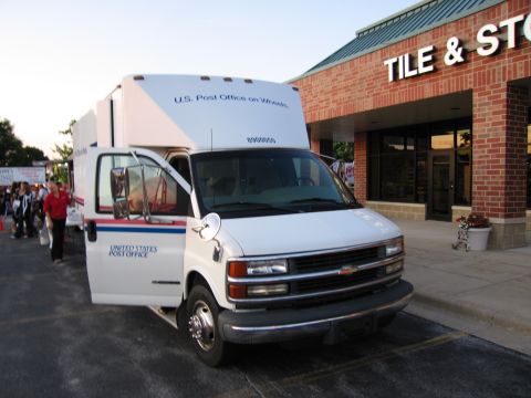 1991 Ford Crown Victoria - A white U.S. Post Office van is parked in front of a store with its driver's side door open.