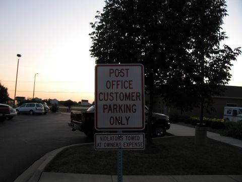 1991 Ford Crown Victoria - A sign indicates customer parking is for the post office only, with a notice that violators will be towed at their own expense.