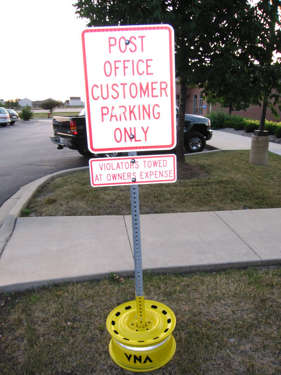 "Post Office Customer Parking Only" sign mounted on a post in a yellow wheel-rim base