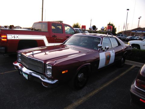 1991 Ford Crown Victoria - A maroon police car is parked next to a red pickup truck.