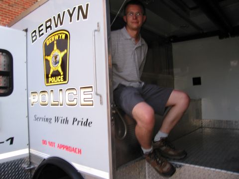 1991 Ford Crown Victoria - Man sits in the doorway of a Berwyn Police vehicle, which has 'Serving With Pride' text on its side.
