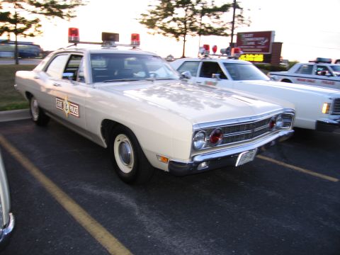 1991 Ford Crown Victoria - A vintage police car with a distinctive grille and dual red lights on its roof is parked in a lot.