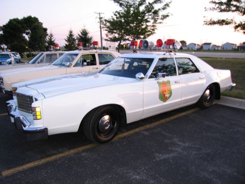 1991 Ford Crown Victoria - Two older model police cars are parked side-by-side in a parking lot at dusk.