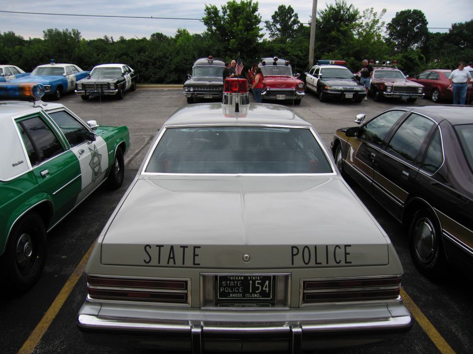 Rear of tan STATE POLICE sedan, RI plate 154, green cruiser at left