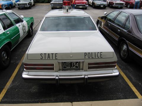 1991 Ford Crown Victoria - A light-colored police car is parked next to other vehicles, showing its rear end with 'STATE POLICE' text and a license plate.