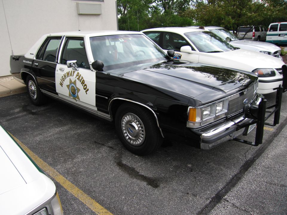 Black and white CHP Highway Patrol Ford sedan with star door emblem, parked