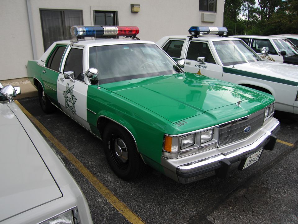 Green and white Sheriff Ford sedan with star emblem and lightbar in lot