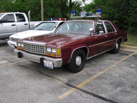 1991 Ford Crown Victoria - A maroon 1991 Ford Crown Victoria police car is parked next to a white pickup truck and another police car.