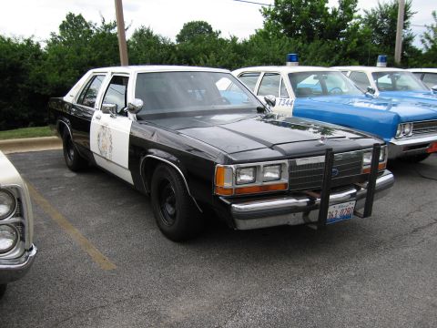 1991 Ford Crown Victoria - This police car has a two-tone paint scheme and a push bumper, with other police vehicles behind it.