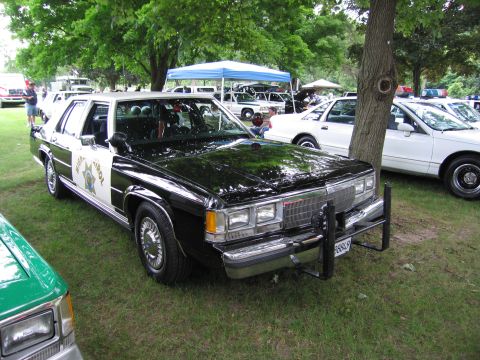 1991 Ford Crown Victoria - A vintage police car is displayed outdoors, with other vehicles and tents in the background.