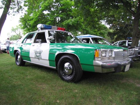1991 Ford Crown Victoria - This sheriff's car, likely from the 1980s, is parked on grass with other vehicles visible in the background.