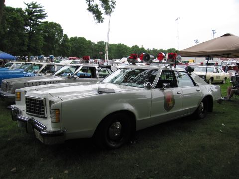 1991 Ford Crown Victoria - Several vintage police cars are displayed on a grassy field under a cloudy sky.