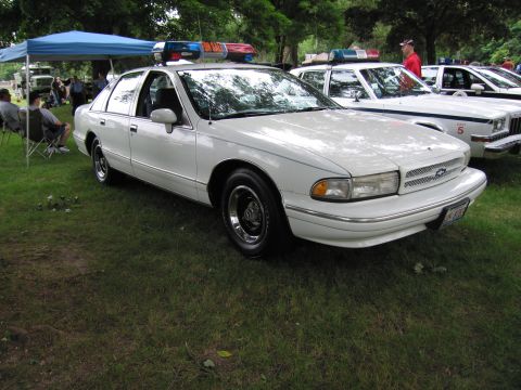 1991 Ford Crown Victoria - A white 1991 Ford Crown Victoria police car is parked on the grass next to other vehicles.