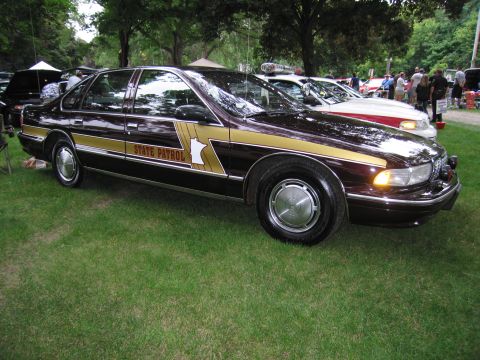 1991 Ford Crown Victoria - A Minnesota State Patrol car is parked on a grassy area, with other vehicles and people in the background.