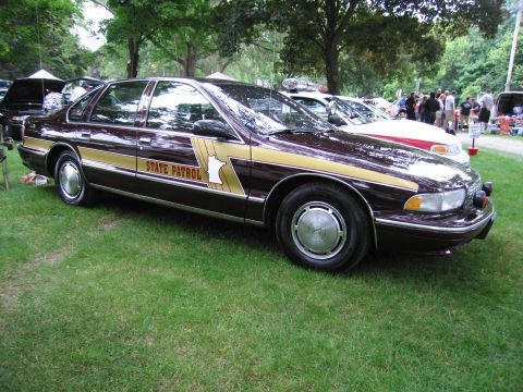 1991 Ford Crown Victoria - A 1991 Ford Crown Victoria, marked as a State Patrol vehicle, is displayed outdoors with other cars and people in the background.