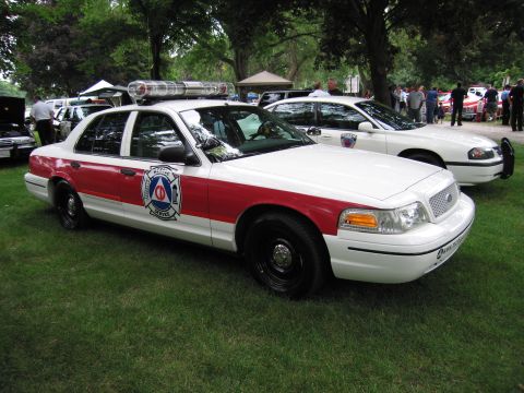 1991 Ford Crown Victoria - A white and red police car with a light bar is parked on grass next to another police car.