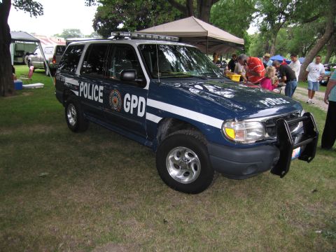 1991 Ford Crown Victoria - A police SUV is parked on grass with people in the background near tents.