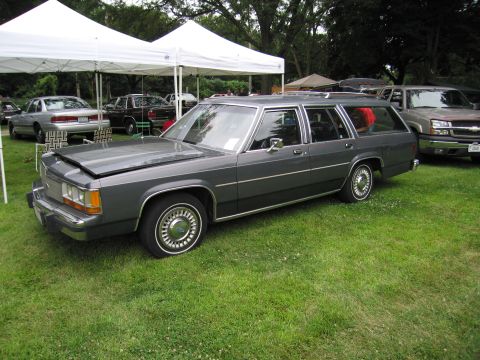 1991 Ford Crown Victoria - A 1980s Ford Country Squire station wagon is parked on the grass with its hood open, alongside other vehicles.