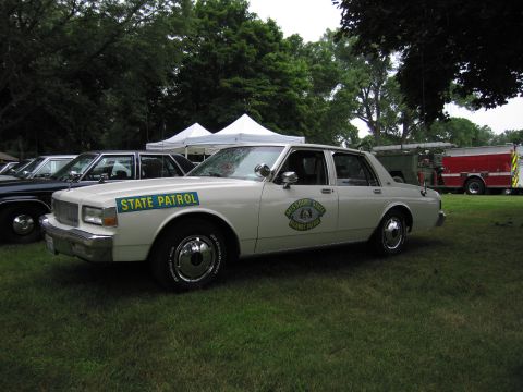 1991 Ford Crown Victoria - A white Missouri State Highway Patrol car is parked on grass with other vehicles and tents in the background.