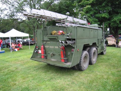 1991 Ford Crown Victoria - A large, olive-drab fire truck with dual rear wheels and a prominent ladder is displayed outdoors.