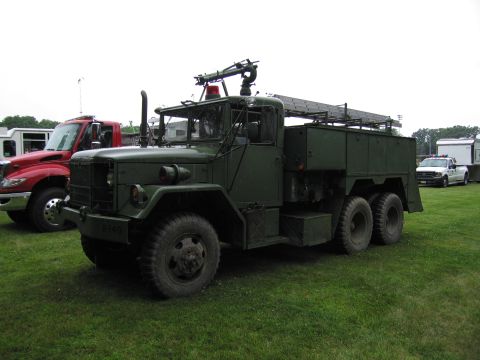 1991 Ford Crown Victoria - A green military truck with a water cannon is parked on grass, with a red truck and a white pickup truck visible in the background.