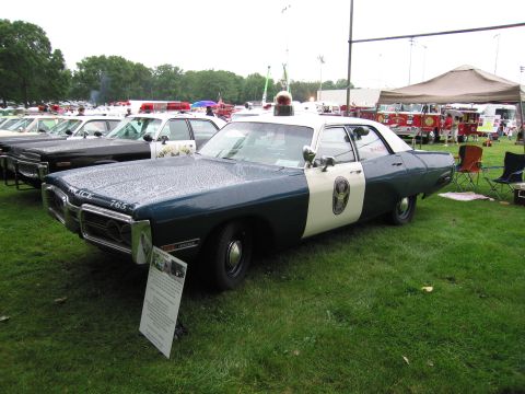 1991 Ford Crown Victoria - A two-tone police car is displayed on a grassy field with other vehicles and tents in the background.