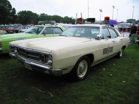 1991 Ford Crown Victoria - A vintage police car, likely a 1969 Ford, is parked on a grassy field next to another police vehicle.