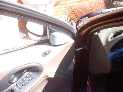 1999 Ford Taurus - Open car door revealing the interior door panel with four-button power window switch, side mirror, and beige headliner trim.