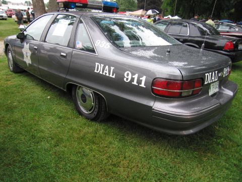 1991 Ford Crown Victoria - This police car, marked with "DIAL 911" and a light bar, is parked on grass next to other vehicles.