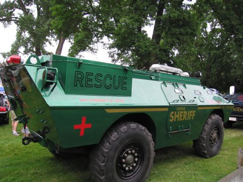 1991 Ford Crown Victoria - A green armored vehicle marked "RESCUE" and "SHERIFF" is parked on grass with trees in the background.