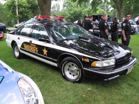 1991 Ford Crown Victoria - A 1991 Ford Crown Victoria police car is parked on grass with other vehicles and people in the background.