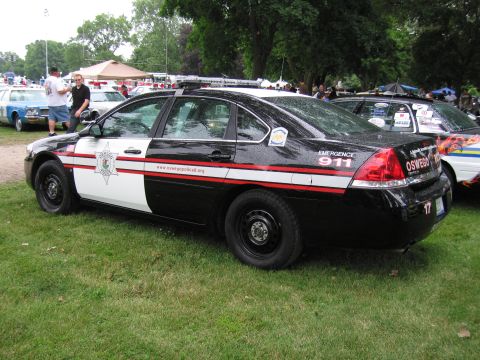 1991 Ford Crown Victoria - A black and white police car is parked on grass, with other vehicles and tents in the background.