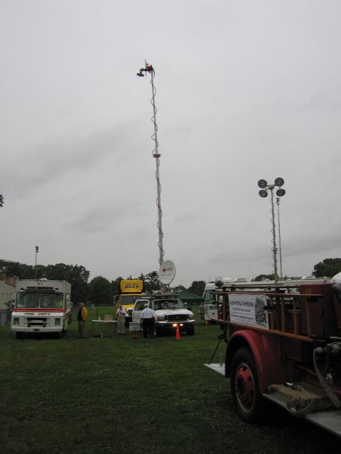 1991 Ford Crown Victoria - A scene with multiple vehicles and communication towers, including a fire truck and utility trucks, set up on a grassy field under an overc…