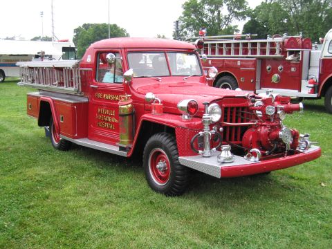 1991 Ford Crown Victoria - A red fire truck with a ladder and pump is parked on grass next to another fire truck.